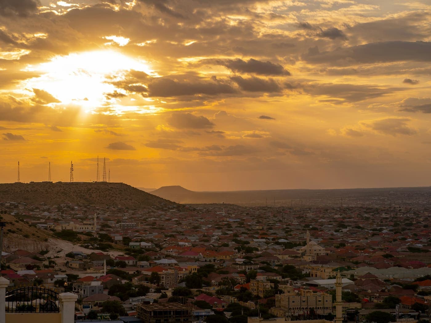 A city spread beneath low hills at sunset, minarets rising among the rooftops