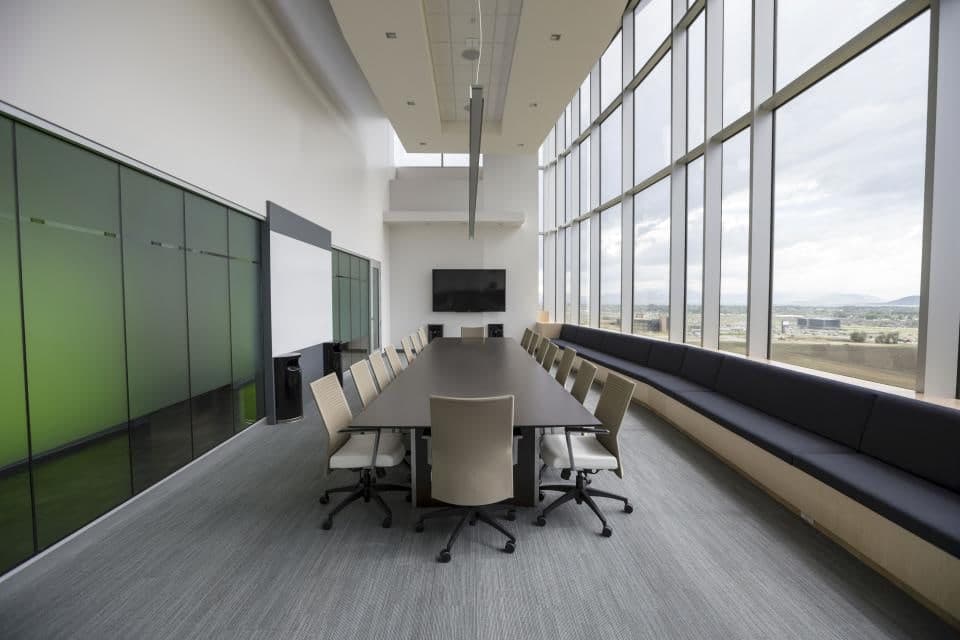An empty conference room set for a roundtable, with a long table and daylight down one wall